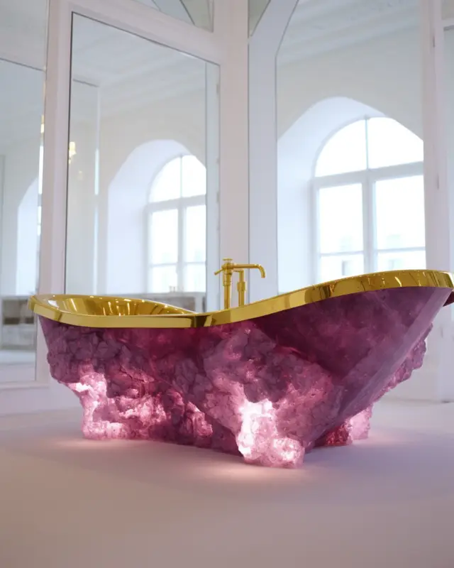 Translucent magenta gemstone bathtub with glowing base and gold-rimmed interior in a grand white room